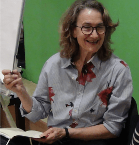 Kate Jobe, smiling, wearing glasses and holding a pen and notebook
