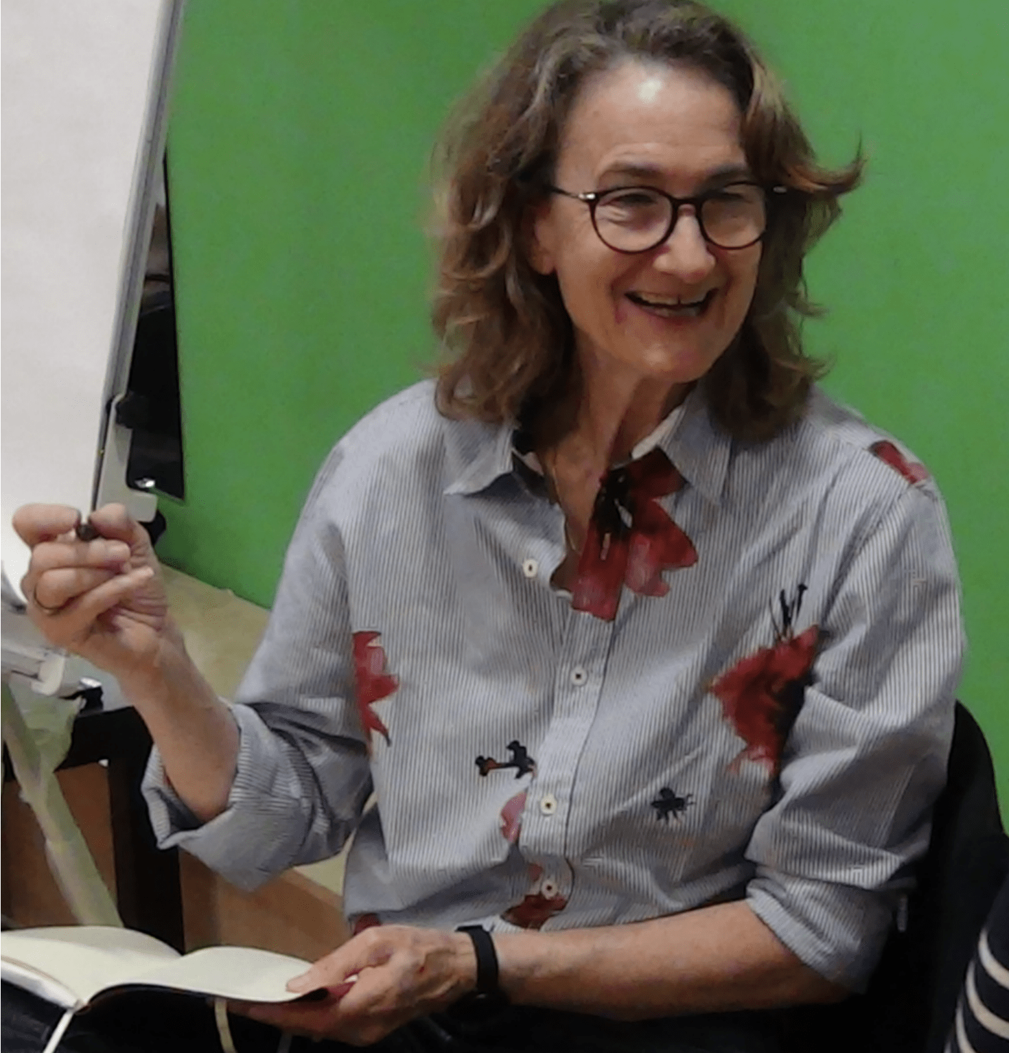 Kate Jobe, smiling, wearing glasses and holding a pen and notebook